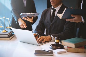 Business professionals in suits working on a laptop with legal books, scales of justice, and a gavel on the table.
