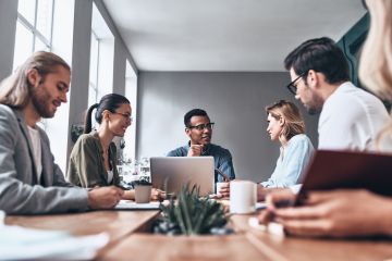 Diverse group of professionals engaged in a discussion around a table in a modern office setting.