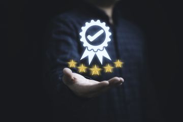 Success: hand holding a digital badge with a checkmark above five gold stars, symbolizing quality or excellence.