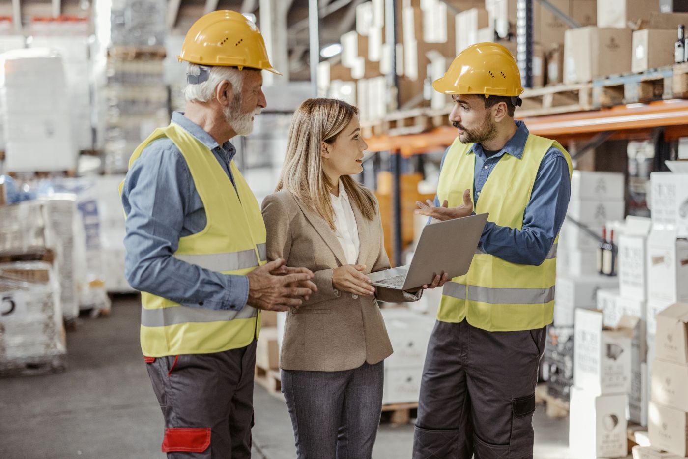 Warehouse staff in discussion wearing hi vis jackets and helmets.