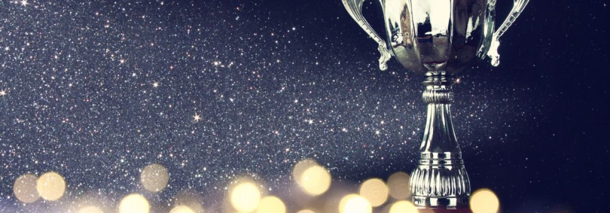Silver trophy cup on wooden surface with sparkling lights and glittering background celebrating success.